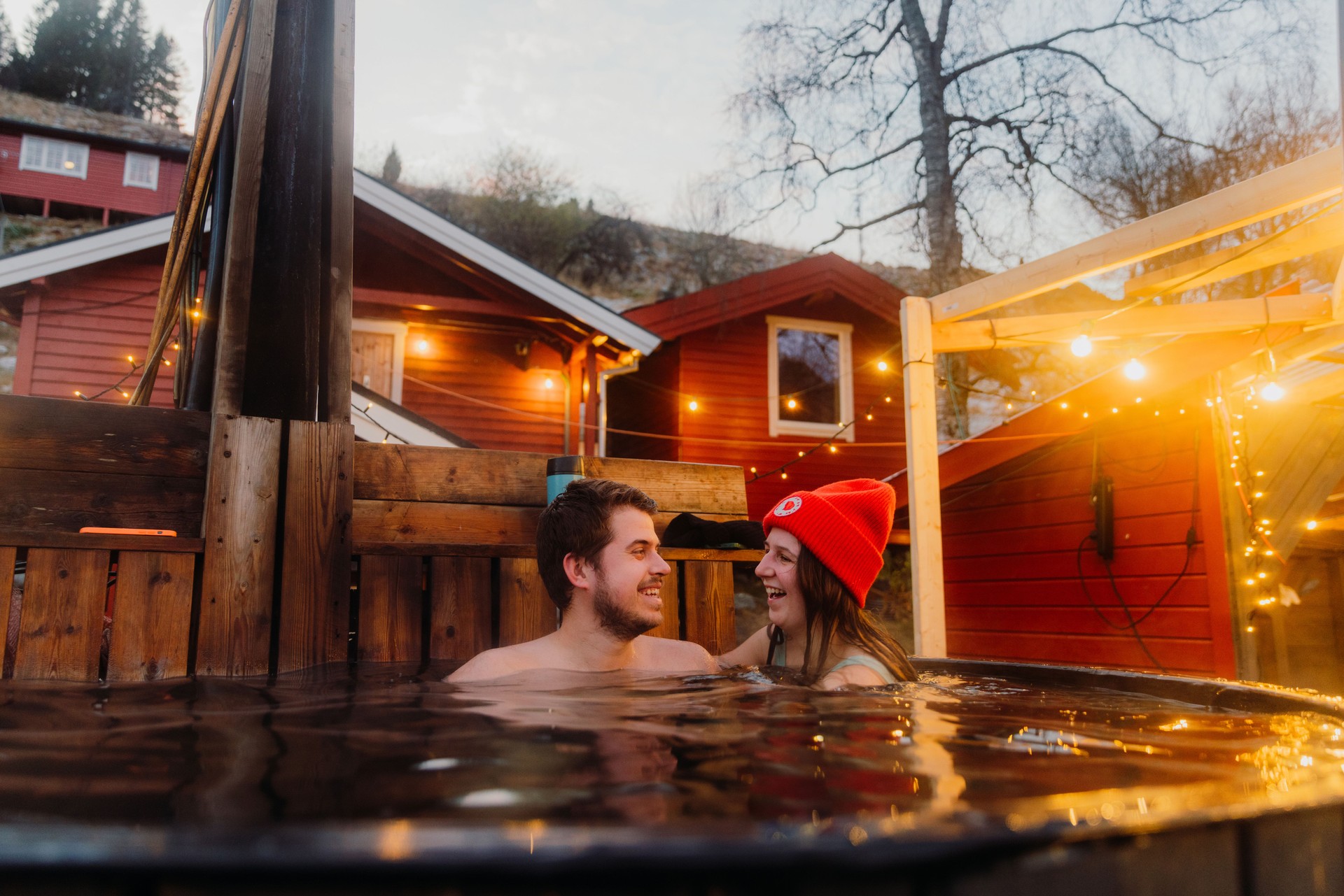 Happy woman and man relaxing in hot tub with scenic mountain view by the fjord in winter in Norway